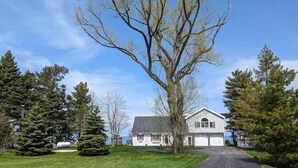 Une maison à deux étages avec un garage, entourée d’une pelouse bien entretenue et d’arbres.