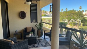 Un espacio exterior techado con mobiliario de mimbre, ventilador de techo y vistas a un jardín ajardinado.