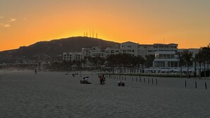 Escena de playa con edificios al fondo y un atardecer.