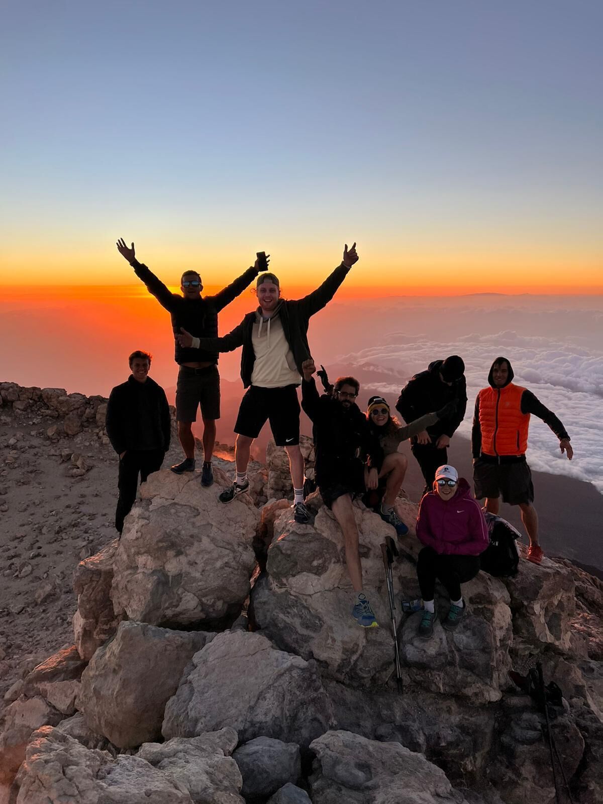 Un grupo de personas sobre un afloramiento rocoso, con el atardecer de fondo.