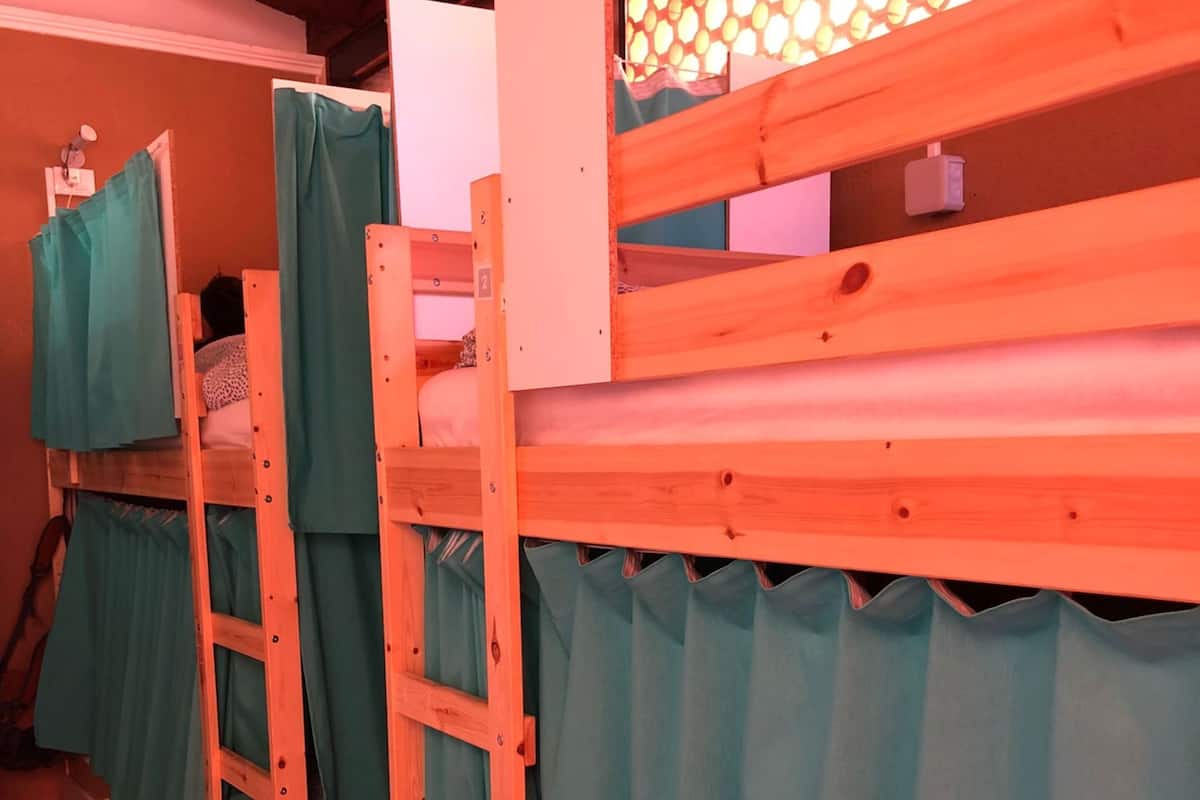A row of bunk beds with green curtains, a white cabinet, and a honeycomb light fixture.
