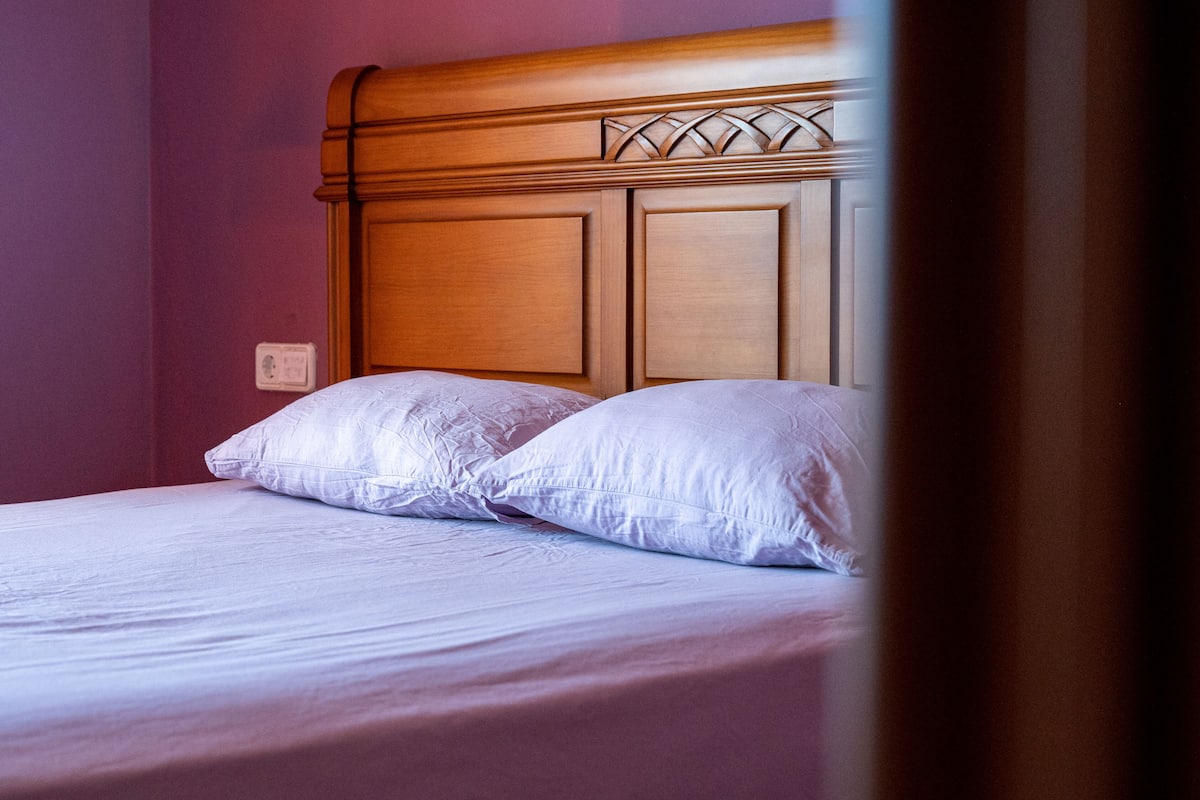 A bed with a wooden headboard, two pillows, and a purple wall.