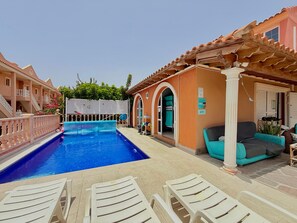 A pool area with lounge chairs, a covered seating area, and a building with a tiled roof. - Duque Nest Hostel (Adeje)