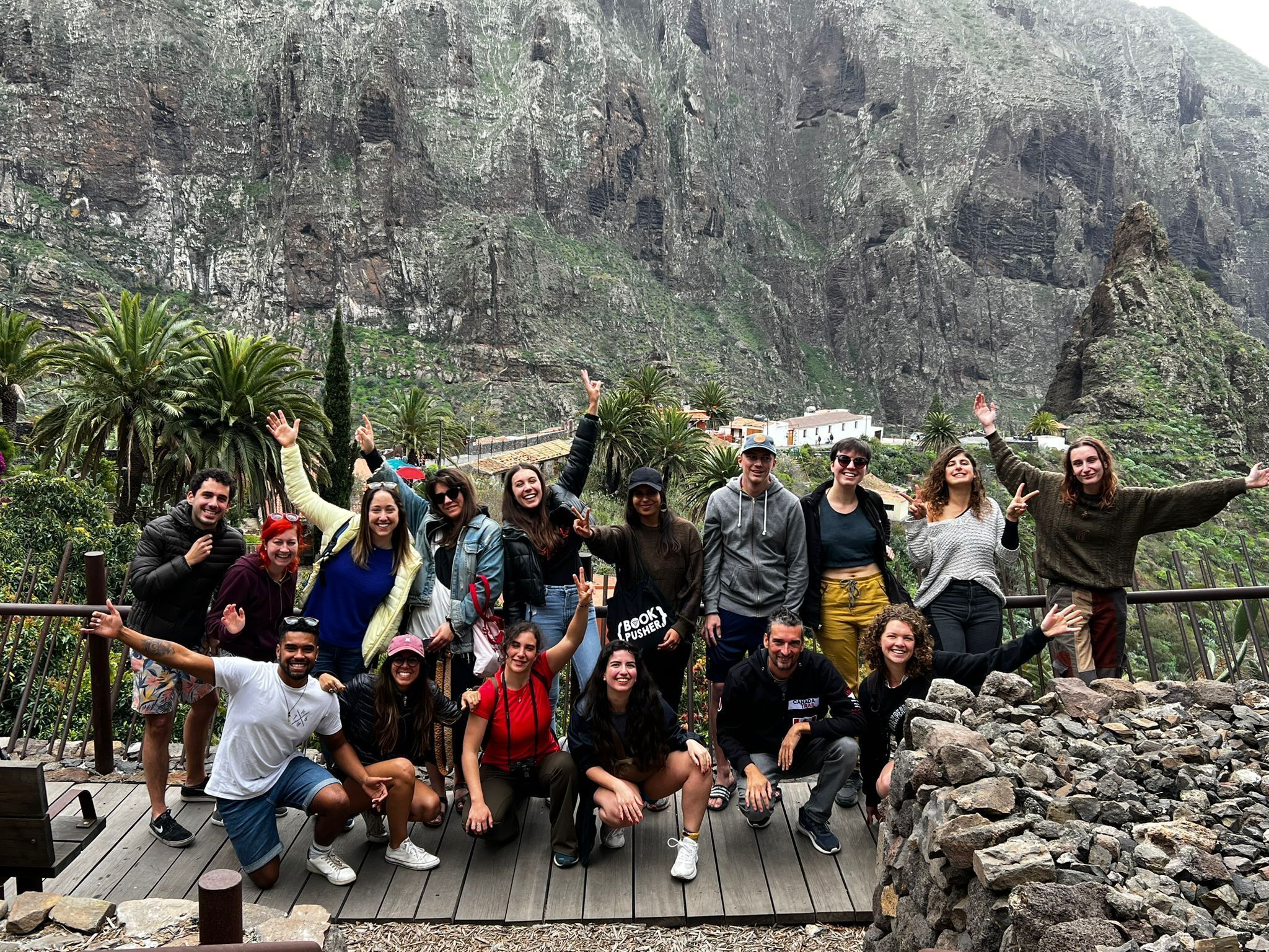 A group of people posing on a wooden deck with a mountainous backdrop.