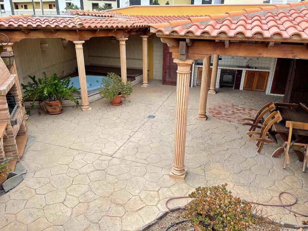 Un patio con baldosas hexagonales, una piscina, plantas en macetas y mobiliario de madera.