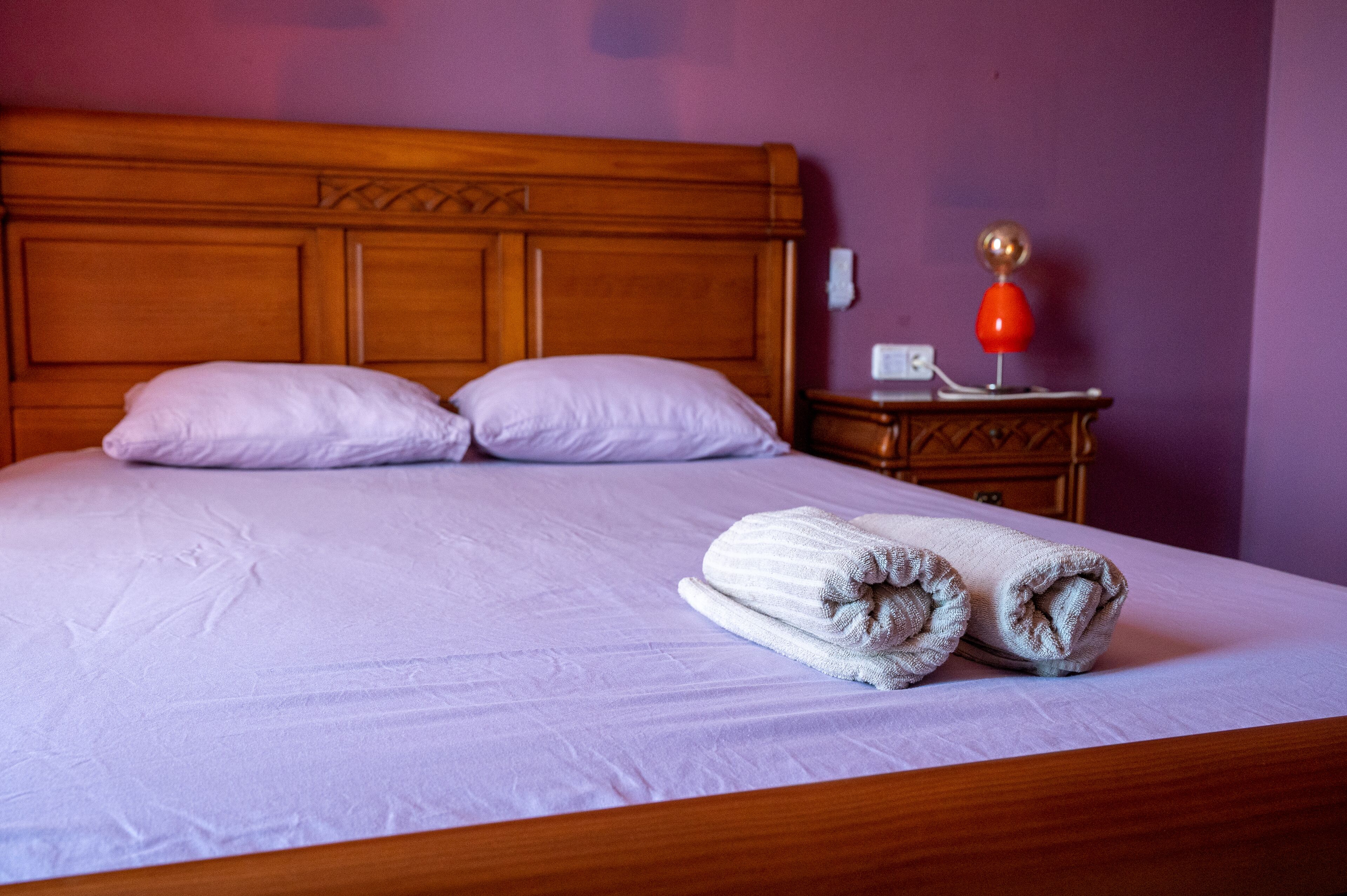 A neatly made bed with two pillows, a wooden headboard, and a nightstand with a lamp.
