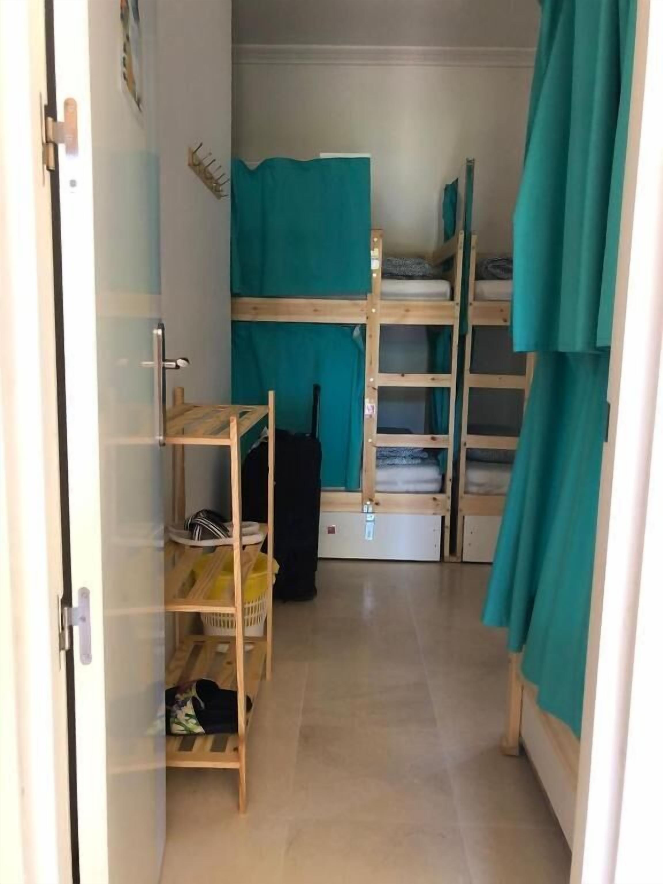 A compact room with bunk beds, a small shelf unit, and a door.