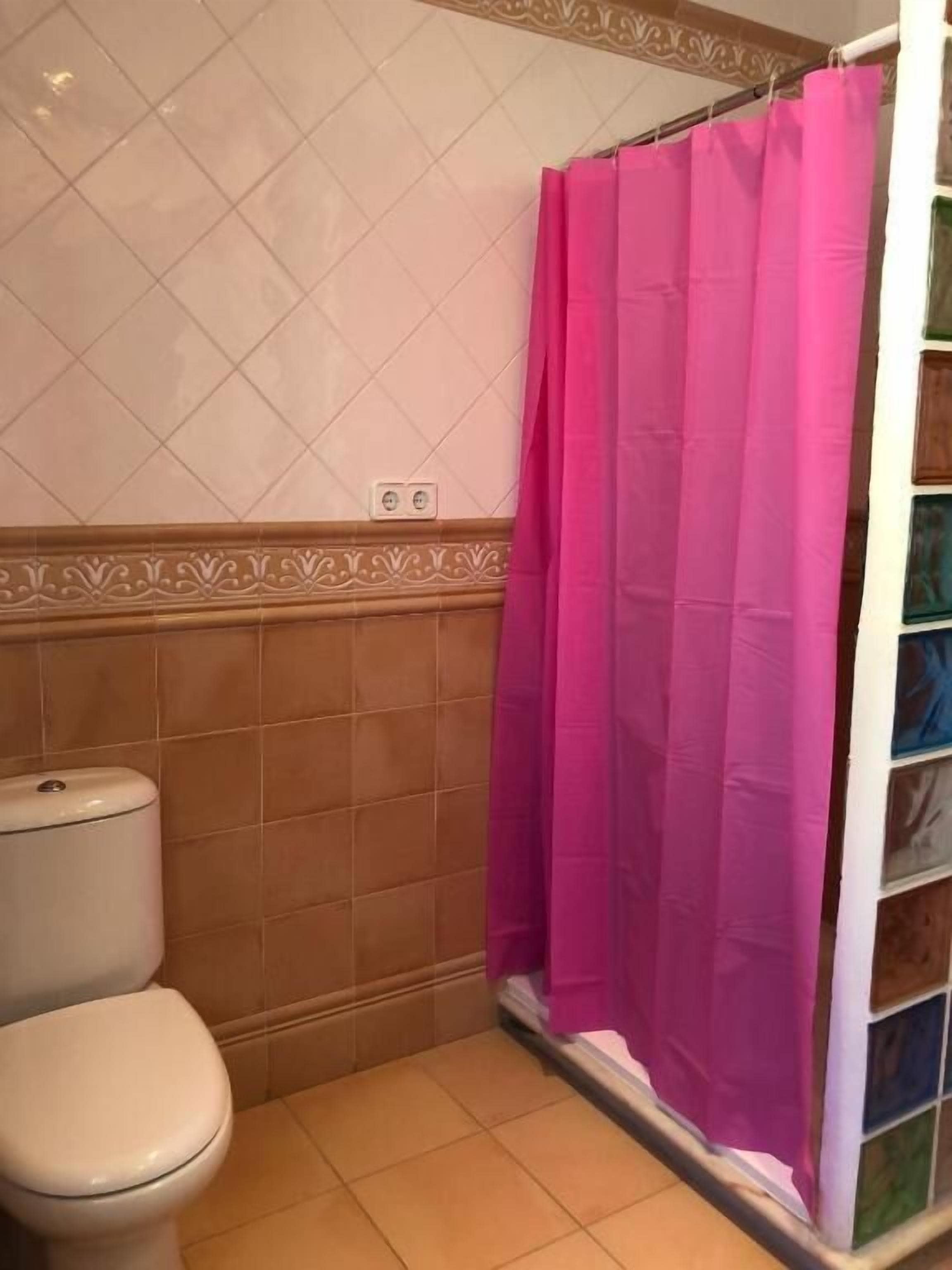 Un baño con inodoro, cortina de ducha y paredes de azulejos.