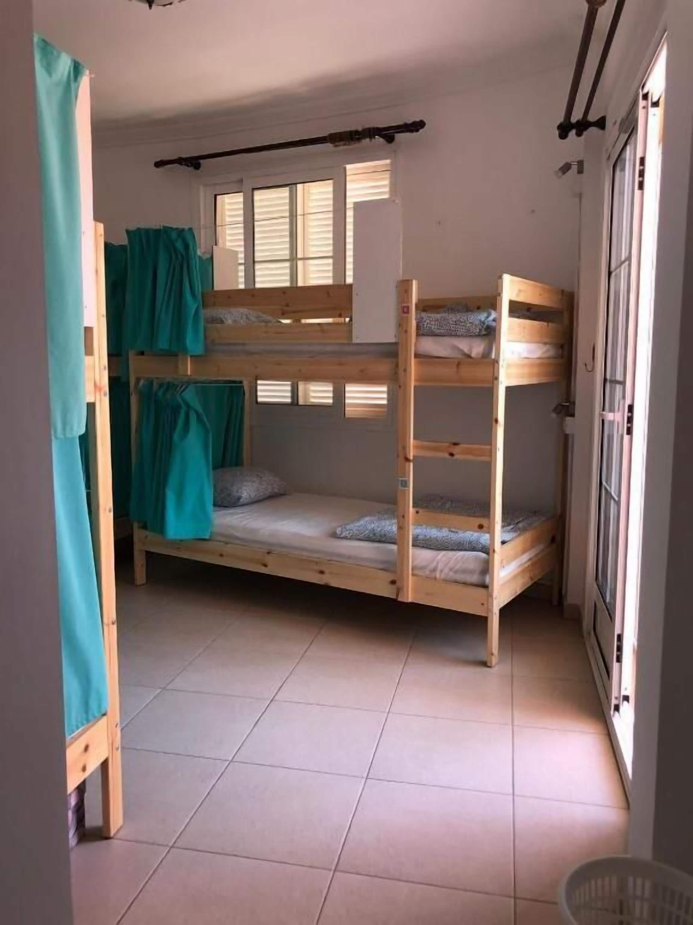 Dormitorio con literas, una ventana, cortina y suelo de baldosas.