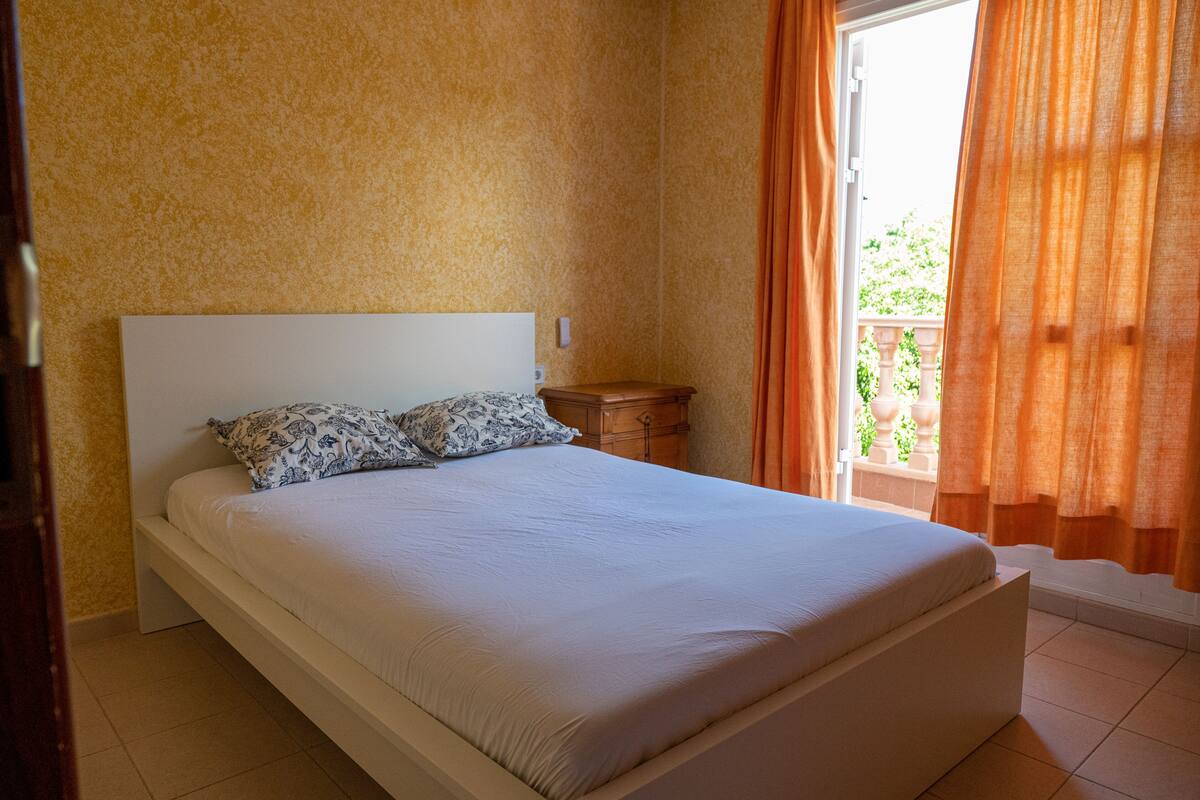 A bedroom with a bed, a nightstand, and a window with curtains.