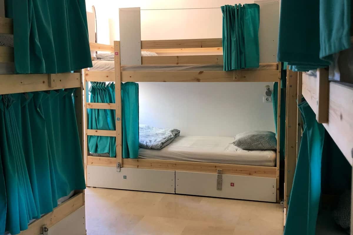 A bunk bed room with teal curtains, a wooden ladder, and a tiled floor.