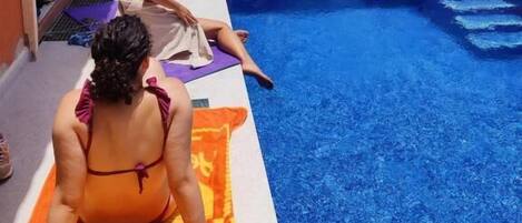 Zona de piscina con gente tomando el sol y relajándose.