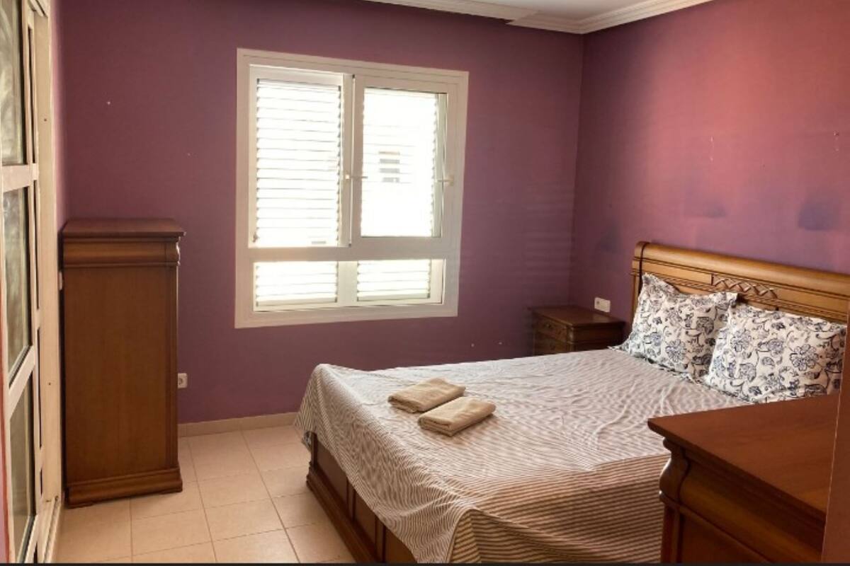 A bedroom with a bed, a nightstand, a dresser, and a window with blinds.