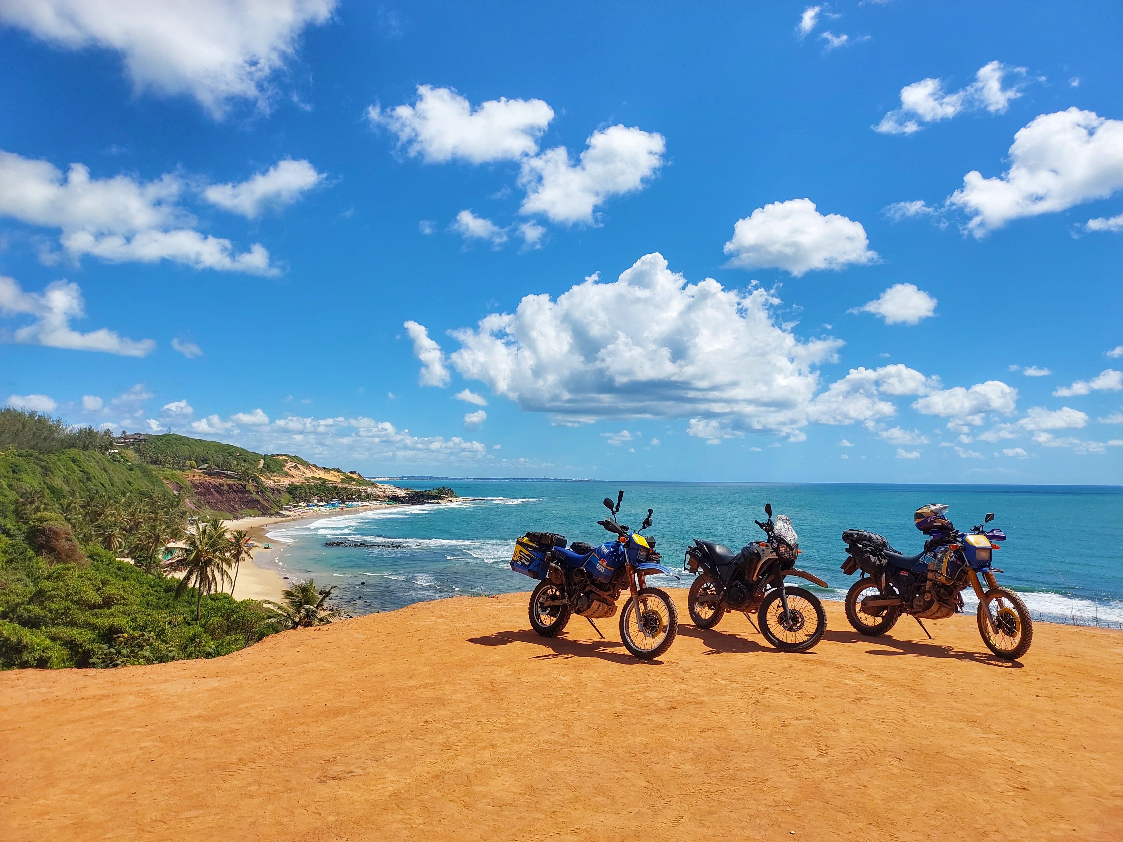 A beach with motorcycles parked on the sand, overlooking the ocean and a clear sky.