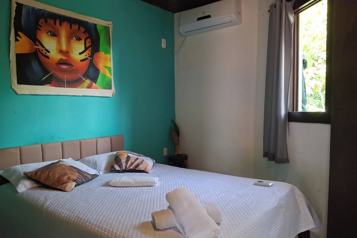 A bed with white bedding, a pillow, and a rolled towel.