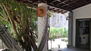A hammock tied to a tree, a straw hat hanging on a post, and potted plants in a covered outdoor area. - Pousada Toa Toa Em Pipa (Tibau do Sul)