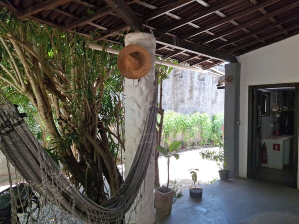 A hammock tied to a tree, a straw hat hanging on a post, and potted plants in a covered outdoor area. - Pousada Toa Toa Em Pipa (Tibau do Sul)