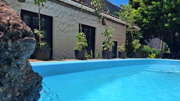 A swimming pool with clear blue water, surrounded by potted plants and a building with large windows. - Pousada Toa Toa Em Pipa (Tibau do Sul)
