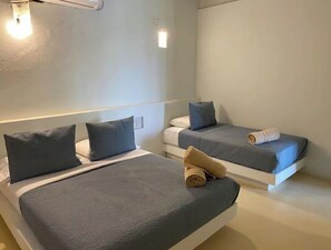 Habitación de hotel con dos camas, cada una con colchón y almohadas azules, y una toalla enrollada sobre una de ellas.