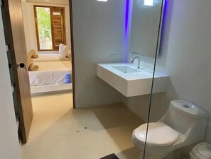 Un baño moderno con lavamanos blanco, inodoro y mampara de vidrio.