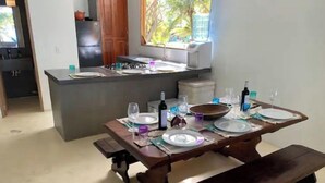 A dining area with a wooden table set for four, a kitchen in the background, and a window with a view of greenery. - ROSARIO ISLANDS, BEACH HOUSE (Cartagena de Indias)