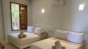 A room with two beds, each with white bedding and rolled towels. There is a window with blinds, a small table, and a wall-mounted air conditioning unit. - ROSARIO ISLANDS, BEACH HOUSE (Cartagena de Indias)
