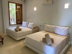 Two single beds with neatly folded towels, a small table, and a chair in a clean, simply designed room.