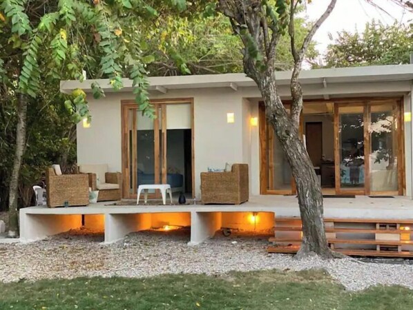 Una casa moderna con un espacio de estar cubierto al aire libre, un banco de madera y un árbol.