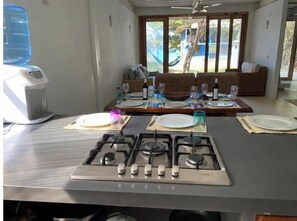 Enjoy meals and relaxation in this kitchen with a gas stove, dining table for four, and large windows offering a view of the outdoor space with a hammock and pool.