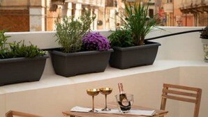 Un balcón con sillas de madera, una mesita pequeña y plantas en macetas.