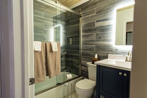 Een moderne badkamer met een douchecabine van glas, een toilet en een wastafel met een spiegel erboven.