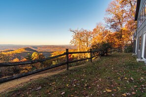 A view from a wooden fence overlooking a valley with autumn foliage, a clear sky, and a building with large windows on the right.