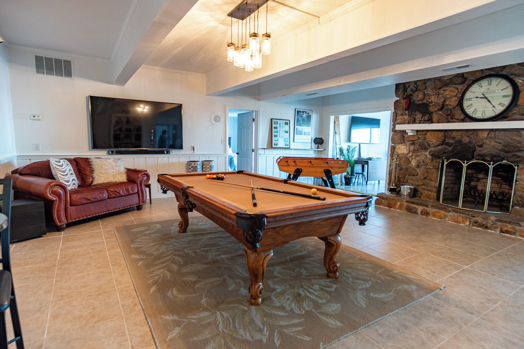 A spacious living room with a pool table, a red leather sofa, a television, and a stone fireplace.