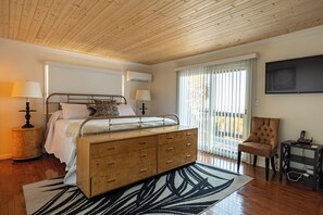 Een slaapkamer met een bed, nachtlampjes, een houten dressoir, een stoel en een televisie aan de muur.