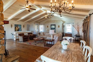 A spacious living room with a wooden ceiling, a dining table, and a cozy seating area.