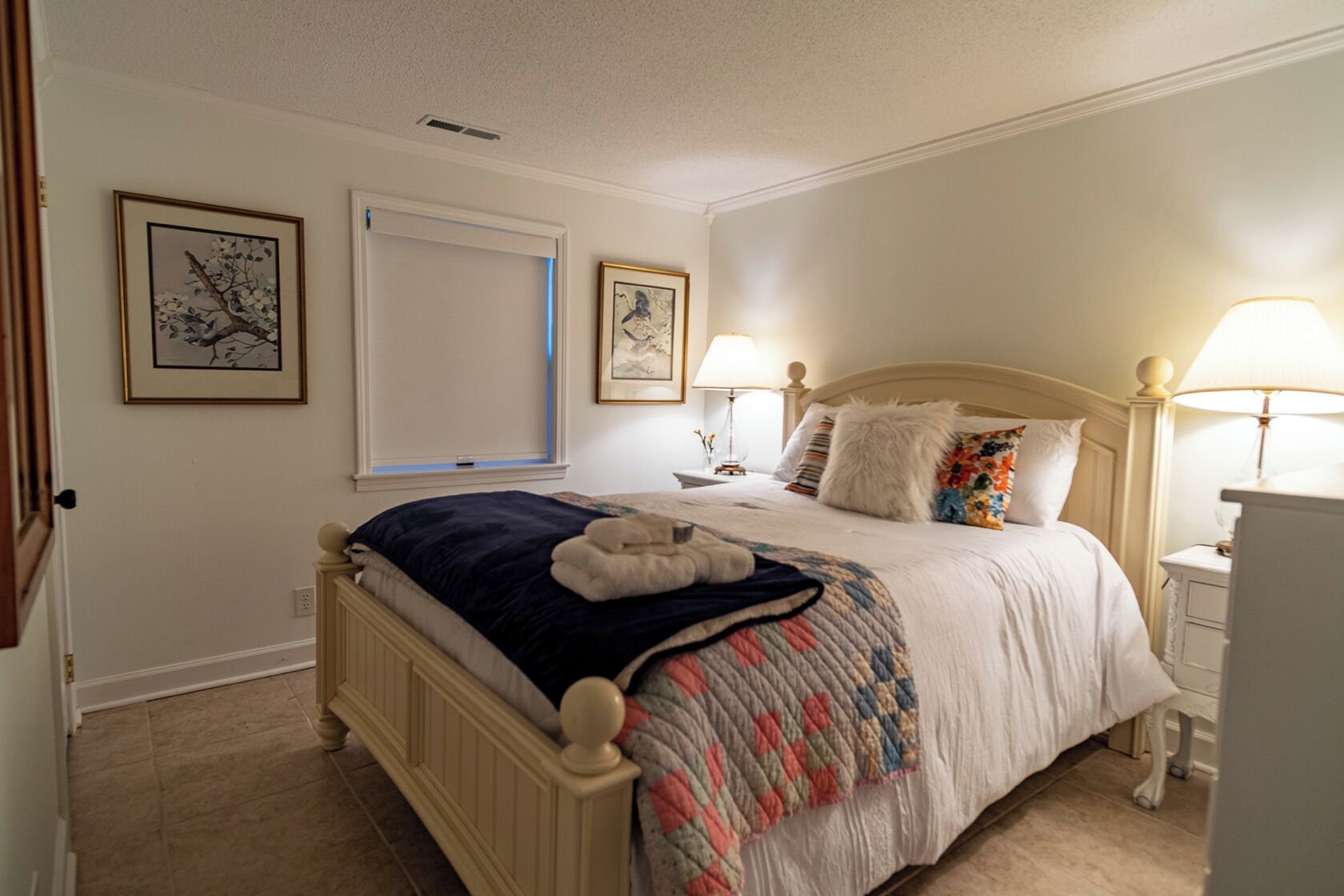 A bedroom with a bed, two bedside tables, a window, and two wall-mounted lamps.