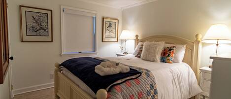 A bedroom with a bed, two bedside tables, a window, and two wall-mounted lamps.