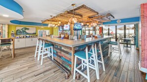 A bar area with a wooden ceiling, bar stools, and a counter with a television screen. - Compass Cove Mariner Tower 624 - Ocean Front Condo - Pools, Lazy River, Hot Tub (Myrtle Beach)