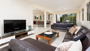Una sala de estar moderna con un televisor de pantalla plana, sofás de cuero, una mesa de centro de vidrio y un área de comedor al fondo.