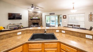 A kitchen with a stone fireplace, granite countertops, wooden cabinets, a ceiling fan, and a dining area with a table and chairs. -  ✨ 4bed 2.5bath Pool Home. 5 mins from WEC! Sleeps 8-10 Guests. Pet Friendly (Ocala)