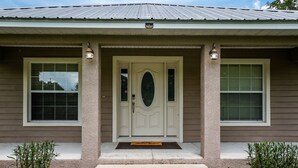 A residential house with a front porch, a central door with a glass panel, and two windows on either side. -  ✨ 4bed 2.5bath Pool Home. 5 mins from WEC! Sleeps 8-10 Guests. Pet Friendly (Ocala)
