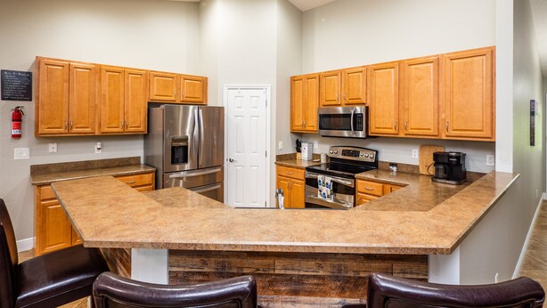 A kitchen with wooden cabinets, stainless steel appliances, a granite countertop, and a built-in island with seating. -  ✨ 4bed 2.5bath Pool Home. 5 mins from WEC! Sleeps 8-10 Guests. Pet Friendly (Ocala)