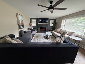 Ein Wohnzimmer mit Sofa, Sesseln, Couchtisch, Kamin und Deckenventilator.