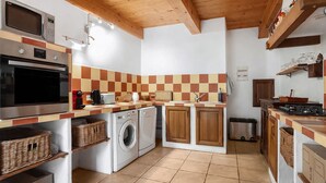 A compact kitchen with a microwave, oven, and washing machine, wooden cabinets, and a tiled backsplash.