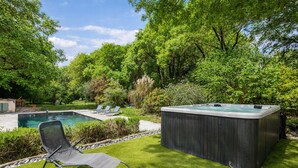 A backyard with a swimming pool, a hot tub, and two lounge chairs.