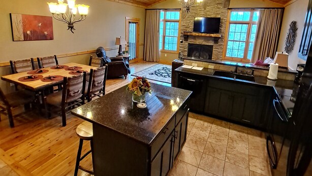 A spacious kitchen with a large island, wooden ceiling, and stone fireplace. - 3A - Comfortable Wooded Setting (Branson)