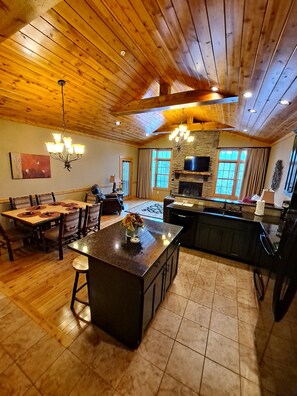 A spacious kitchen with a large island, wooden ceiling, and stone fireplace.
