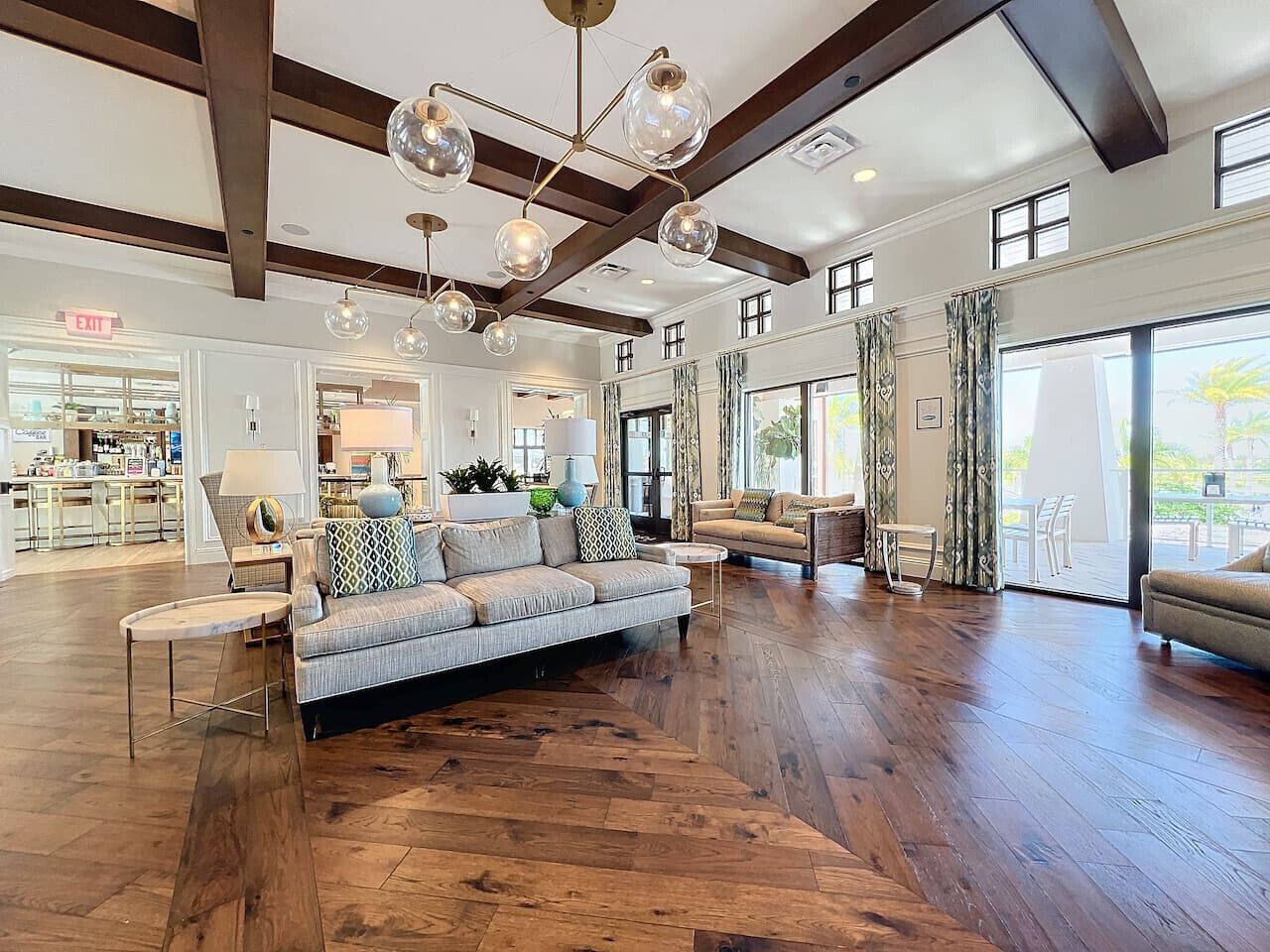 A spacious living area with a large sofa, a coffee table, and a chandelier. There is a kitchen area in the background.