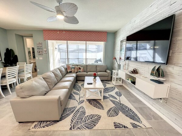 A modern living room with a sectional sofa, a coffee table, and a flat-screen TV mounted on a wooden wall.