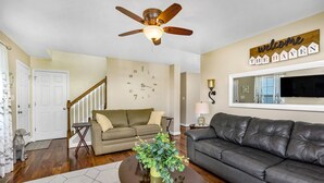 A living room with a ceiling fan, a clock on the wall, a sofa, a coffee table, and a welcome sign. - The Haven, located in the heart of the Shenandoah Valley (Waynesboro)